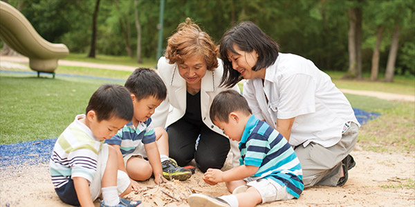 Two woman playing with three kids in the sand at the park